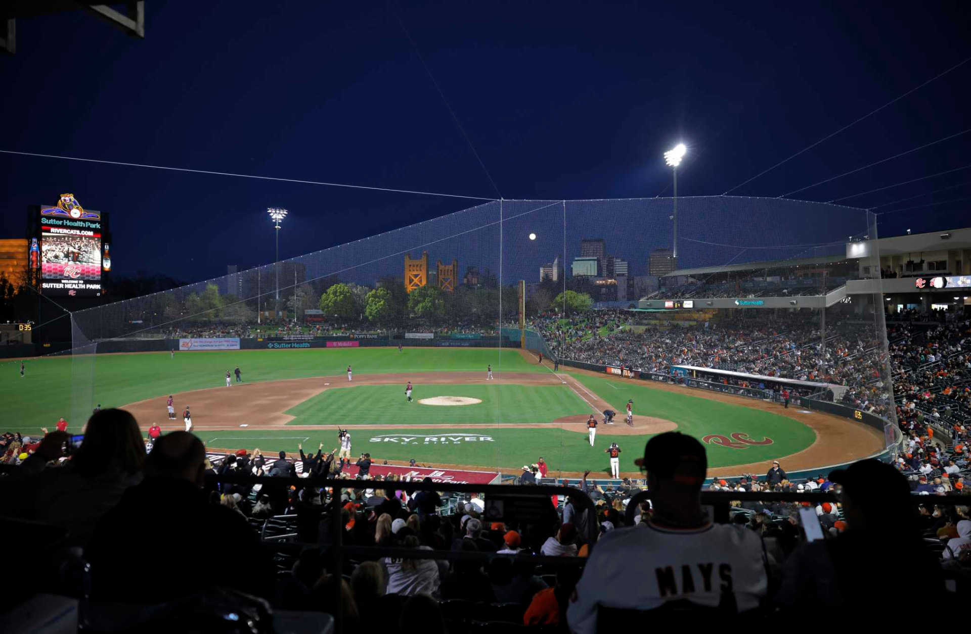 Sutter Health Park baseball stadium at night with the Sacramento skyline and Tower Bridge in the background